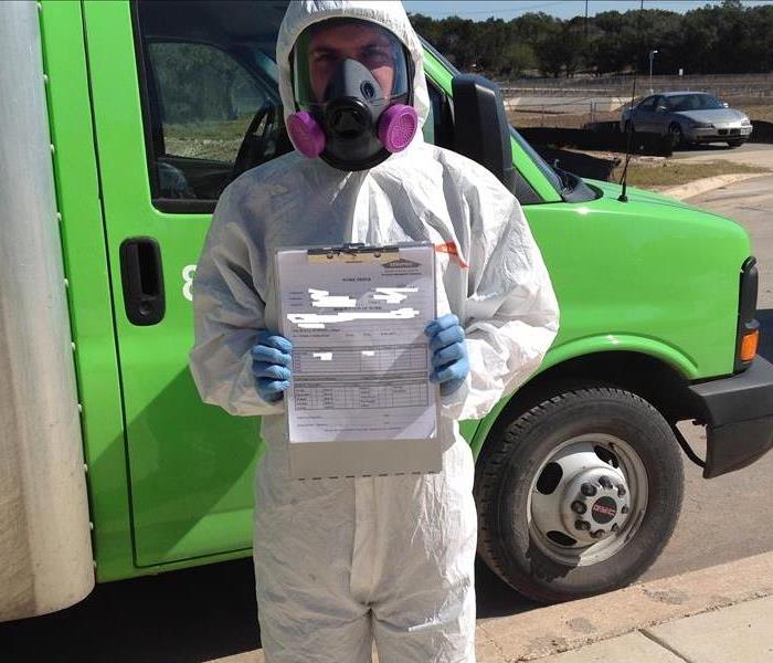 SERVPRO employee in hazmat suit holding up mold certificate